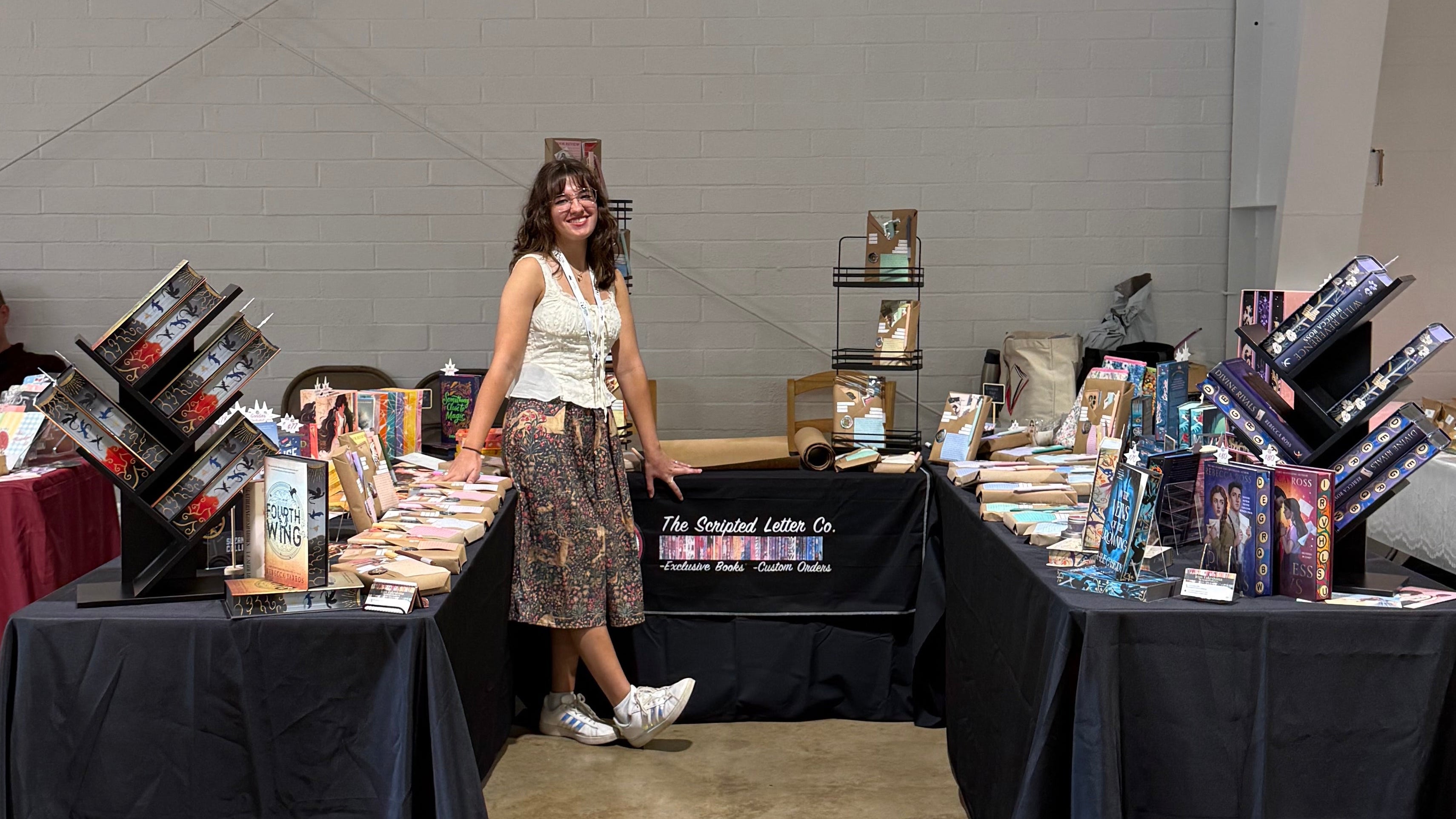 Woman standing between two tables with books in a large indoor space.
